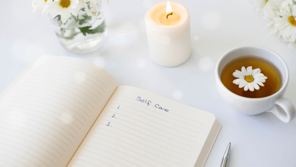 A lit candle, flowers, a cup of tea and a journal 